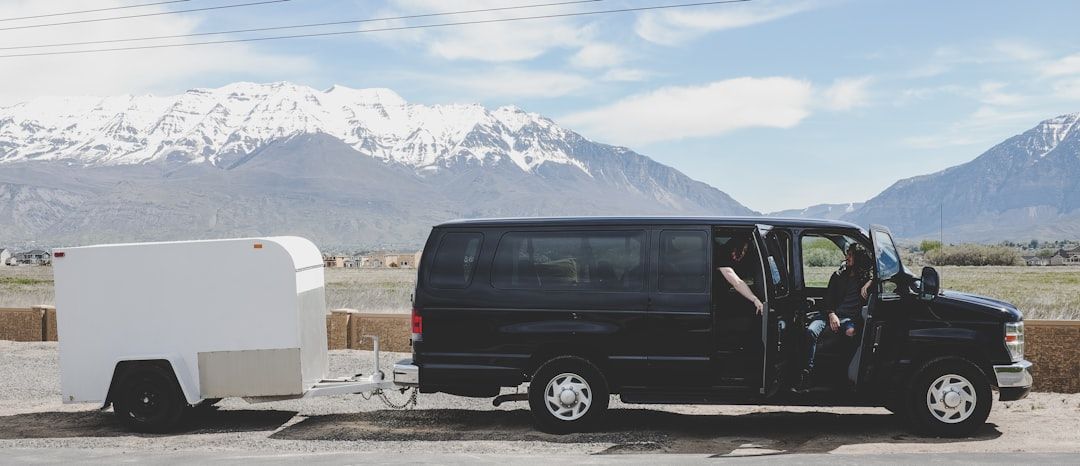 Ein schwarzer Tour-Van mit weißem Anhänger vor einer Bergkulisse.