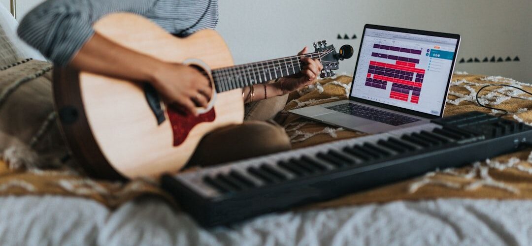 Eine Musikerin nimmt Musik mit Akustikgitarre und Laptop im Bett auf.