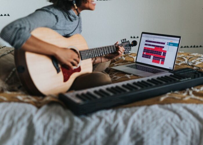 Eine Musikerin nimmt Musik mit Akustikgitarre und Laptop im Bett auf.
