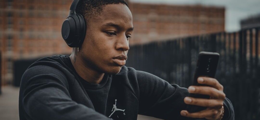Junger Mann mit Kopfhörern betrachtet ein Smartphone beim Musikhören