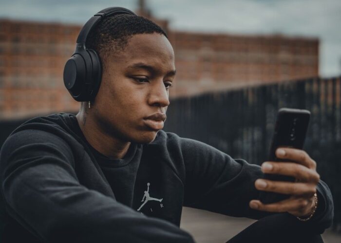 Junger Mann mit Kopfhörern betrachtet ein Smartphone beim Musikhören